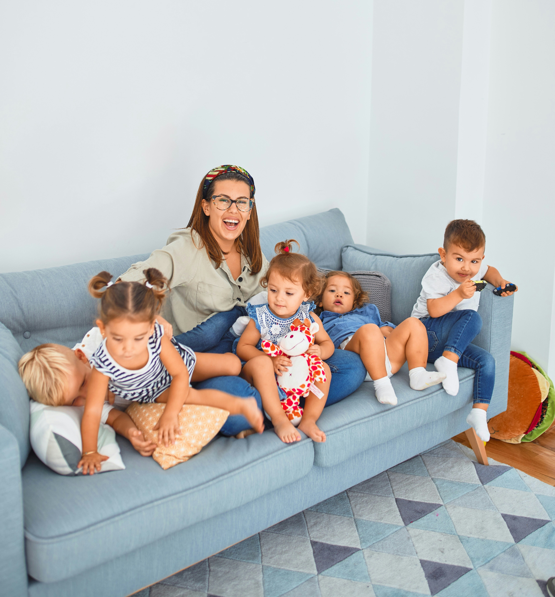 Woman with several children sitting together on a light blue couch in a playful home setting